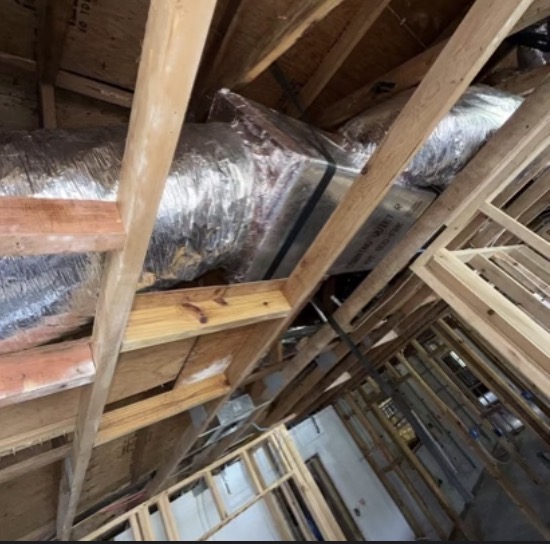 Insulated silver flex ductwork and metal plenum run through wood attic framing